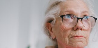 an elderly woman wearing glasses and a pink shirt gazing off in the distance