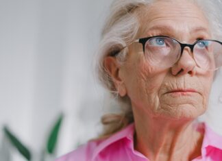 an elderly woman wearing glasses and a pink shirt gazing off in the distance