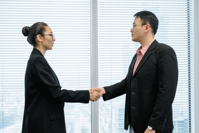 The head of a nonprofit wearing a long black coat shakes hands with a top donor in her office