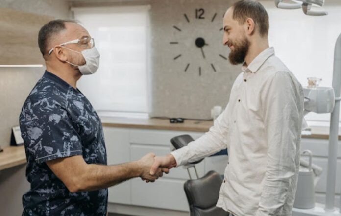 A man in a white shirt shakes hands with a dental hygienist in an examination room